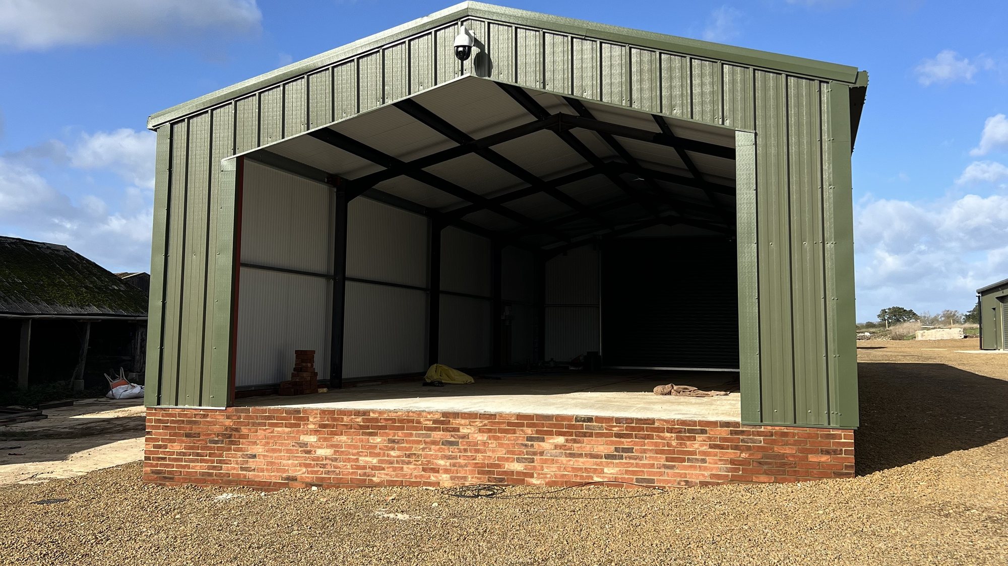 The green barn at Oakcroft Farm with its red brick base, in sunshine